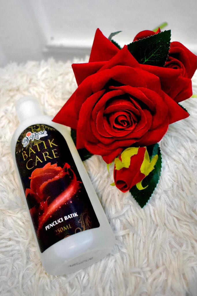 A 250 mL bottle of D'Rose Batik Care batik wash beside a red rose